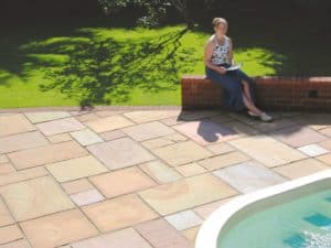 lady sitting on a bench next to the pool surrounded by beige sandstone paving
